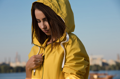 Portrait of confident serious woman under yellow hood over blue sky background