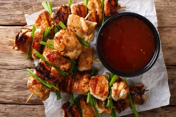 Photo of Asian food: chicken kebab with green onion and chili sauce close-up. horizontal top view