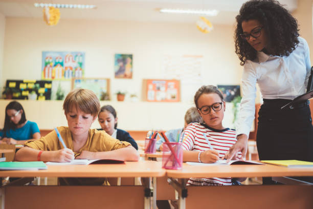 Mixed race teacher helping schoolgirl in class School children in the classroom studying with the assistance of their teacher primary school exams stock pictures, royalty-free photos & images