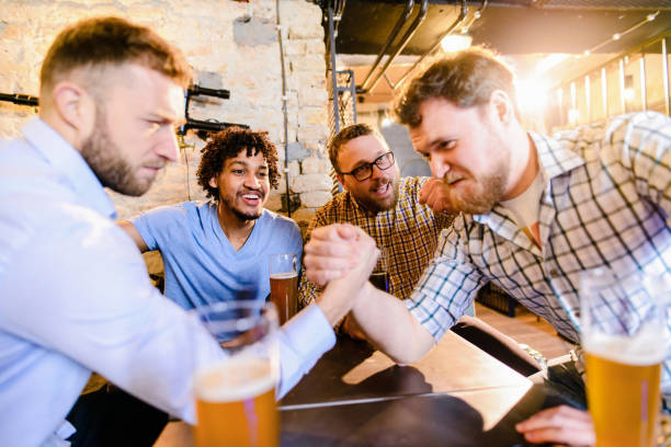 istock Group of mail friends drinking beer in a pub and having fun. Two man arm wrestling while other are supporting. 1043557538