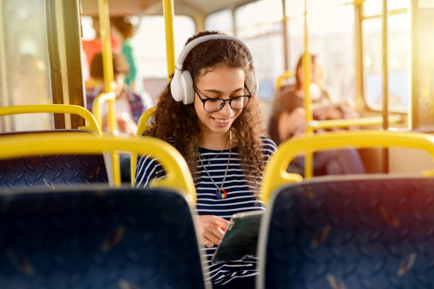 schöne junge lockig studentin in einem bus sitzen und hören die musik auf ihrem weg zur schule. - bussing stock-fotos und bilder