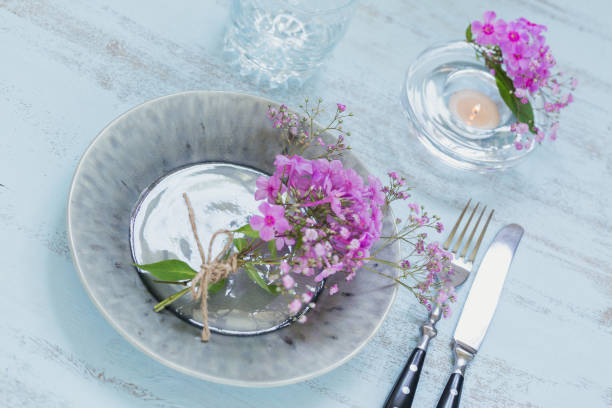 istock Rustic table setting with pink flowers, empty glass and candle on light wooden table. 1043565356