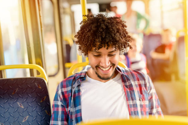 junge glücklich afro-amerikaner in einem bus sitzen und mit blick auf sein telefon. - bussing stock-fotos und bilder