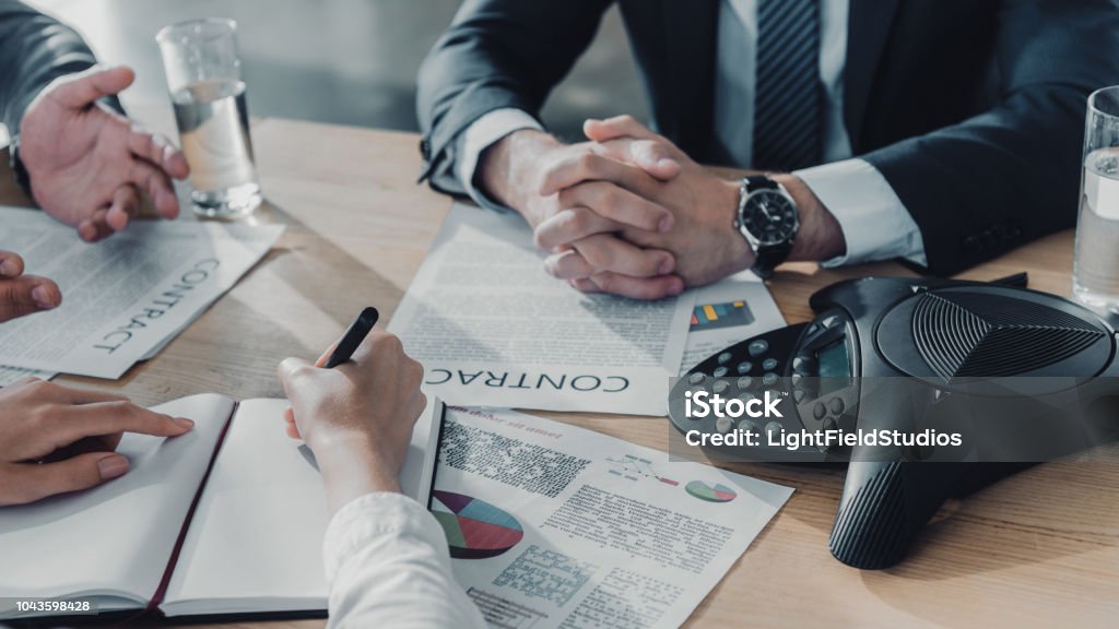 cropped shot of business people having conversation with documents and speakerphone on table at modern office Conference Phone Stock Photo