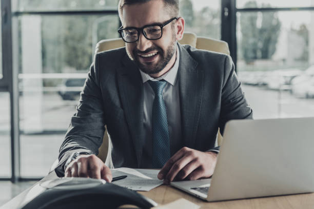 istock handsome smiling businessman using speakerphone at modern office 1043598468
