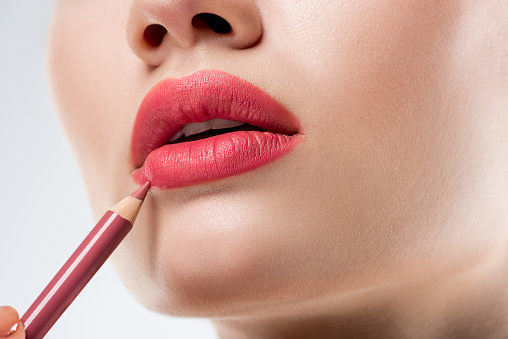 close up studio shot of woman applying lip pencil,  isolated on white