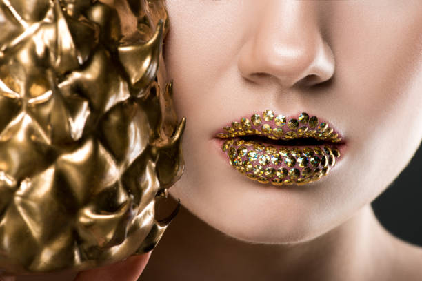 cropped view of woman with gild lips holding golden pineapple recortar vista de mujer con labios de gild con piña de oro