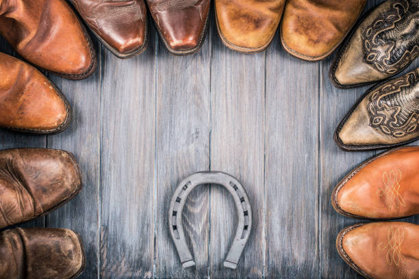 Wild West wooden background concept with retro leather cowboy boots and the horseshoe. Vintage style filtered photo Wild West wooden background concept with retro leather cowboy boots and the horseshoe. Vintage style filtered photo cowboy boot stock pictures, royalty-free photos & images