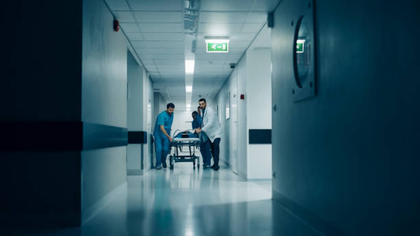 pronto soccorso: medici, infermieri e chirurghi spingono gurney / barella con paziente gravemente ferito verso la sala operatoria. la luce si accende drammaticamente. - emergency room nurse hospital emergency services foto e immagini stock