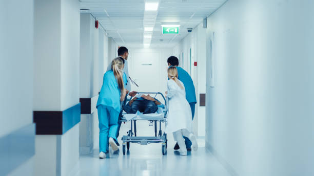 service des urgences : médecins, infirmières et infirmiers poussent gurney / civière avec grièvement blessé patient vers la salle d’opération. hôpital moderne de bright avec le personnel professionnel, sauver des vies. - insurance physical injury transportation healthcare and medicine photos et images de collection