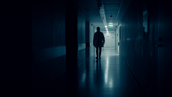 Medical Doctor Silhouette Walks in Dark Part of the Hospital Corridor.