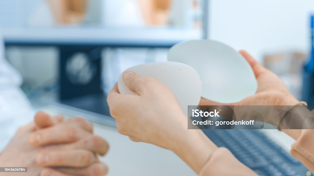 Plastic / Cosmetic Surgeon Shows Female Patient Breast Implant Samples for Her Future Surgery. Professional and Famous Surgeon Working in Respectable Clinic. Breast Implant Stock Photo