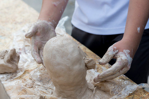 Hands make a man's head from clay, close-up