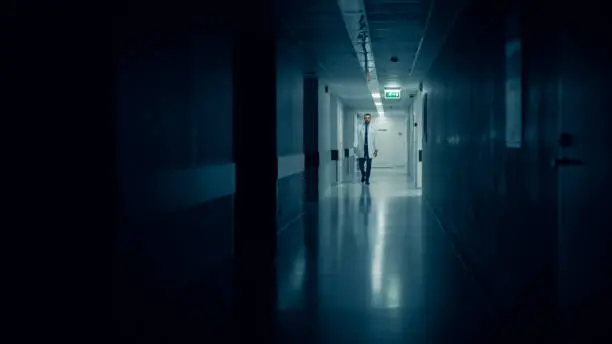 Photo of Medical Doctor Walks into Dark Part of the Hospital Corridor.