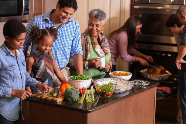 Diverse family in home kitchen cooking Thanksgiving dinner. Multi-ethnic family members work together in grandmother's home kitchen to prepare Thanksgiving dinner.  Hispanic, African and Caucasian ethnicities.  Roasted turkey, vegetable food items. family dinners and cooking stock pictures, royalty-free photos & images