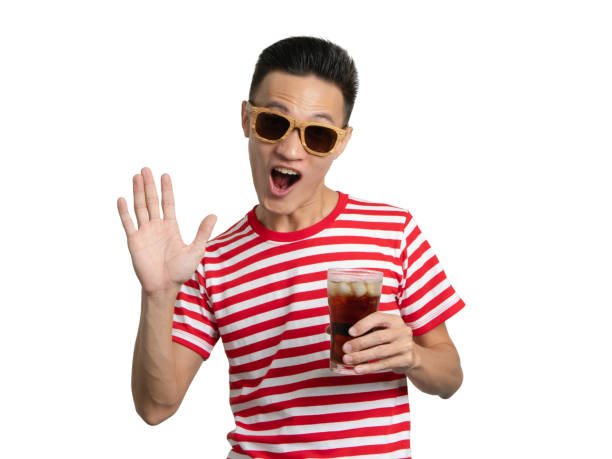 istock Young man holding soft drink shows hand hello greeting. 1043651492