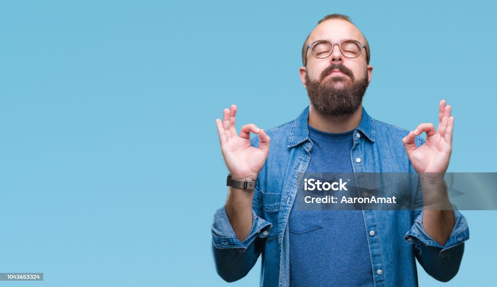 Young caucasian hipster man wearing glasses over isolated background relax and smiling with eyes closed doing meditation gesture with fingers. Yoga concept. Men Stock Photo