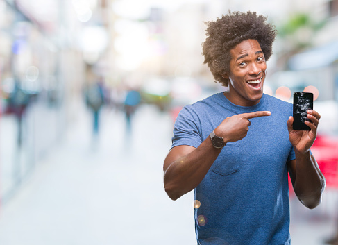 Afro american man holding broken smartphone over isolated background very happy pointing with hand and finger