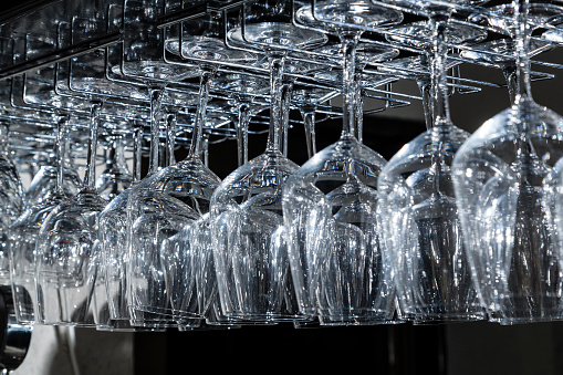 Glass cups arranged and hanging from a bar shelf with background light in the darkness.