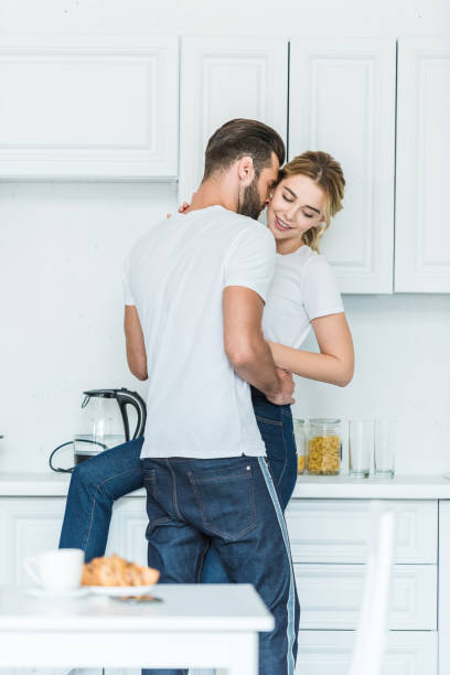 istock handsome young man hugging attractive smiling girlfriend in kitchen 1043658328