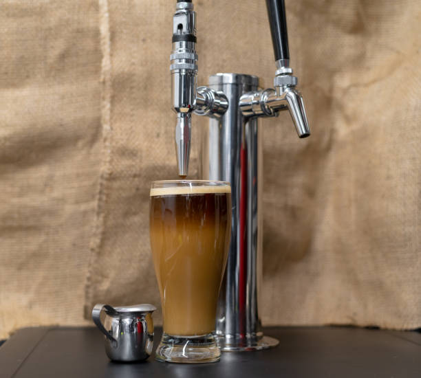 Nitro Cold brew coffee next to a beer style dispensing Tap. Nitrogen infused cold brew coffee in a clear glass next to a tap with sweet cream added and a foamy top. nitrogen stock pictures, royalty-free photos & images