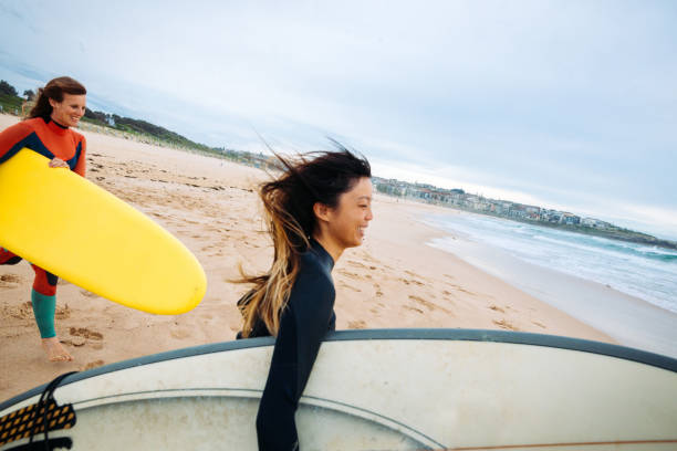 istock Girls rushing into ocean with surf board 1043667512