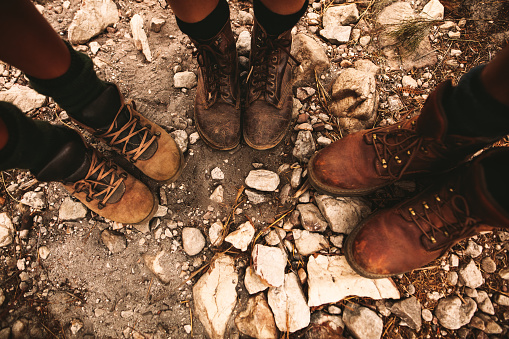 Closeup of hikers shoes on rocky trail. Man and women standing together on rocky path wearing trekking boots.