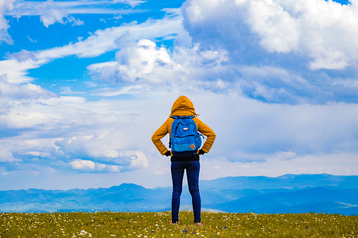 Girl with rucksack on the top of hilly landscape.