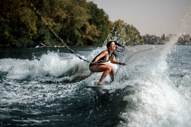 Sexy smiling brunette woman wakesurfing on board down the blue water stock photo
