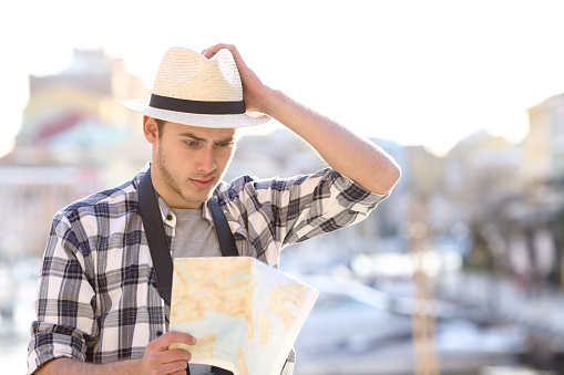 Lost tourist consulting a confusing guide in a coast town street on vacation