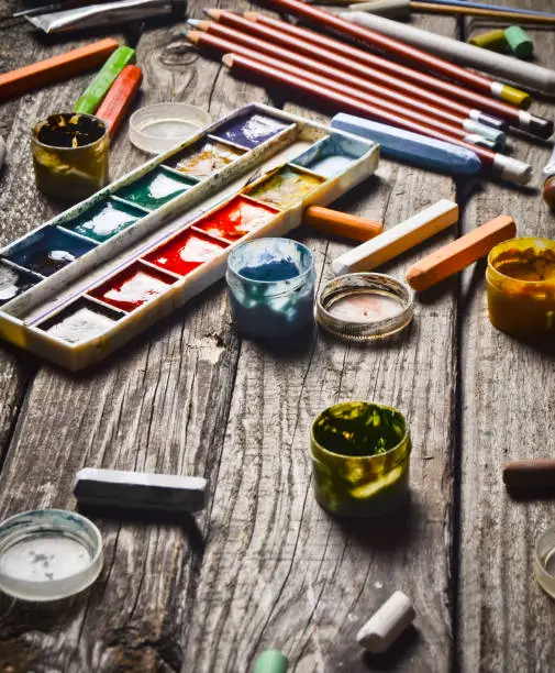 Group of products for drawing and creativity on a wooden table. Rustic style. Gouache, oil painting, watercolor paints, crayons, pencils.