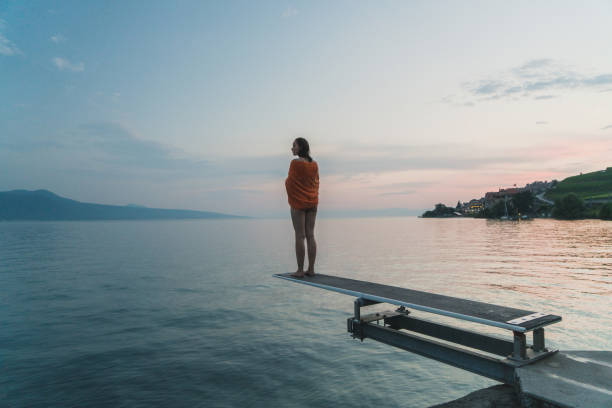 Woman standing on diving board on Geneva lake Young Caucasian woman in orange towel standing on diving board on Geneve lake at sunset geneva switzerland photos stock pictures, royalty-free photos & images