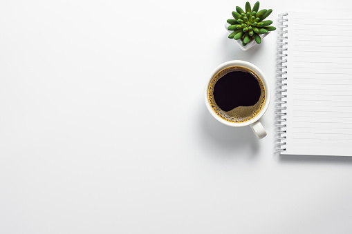 Escritorio de oficina con taza de café, pote del cactus y cuaderno en blanco photo