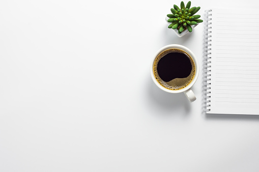 Top view of office desk with coffee cup, cactus pot and blank notebook