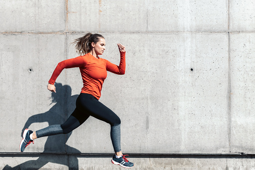 young sportswoman in red sports dress running outdoors in front of concrete wall