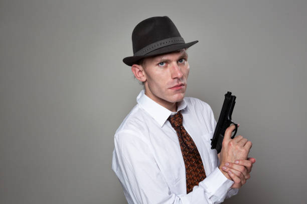 istock young man with hat, white shirt and tie holding gun 1043730274