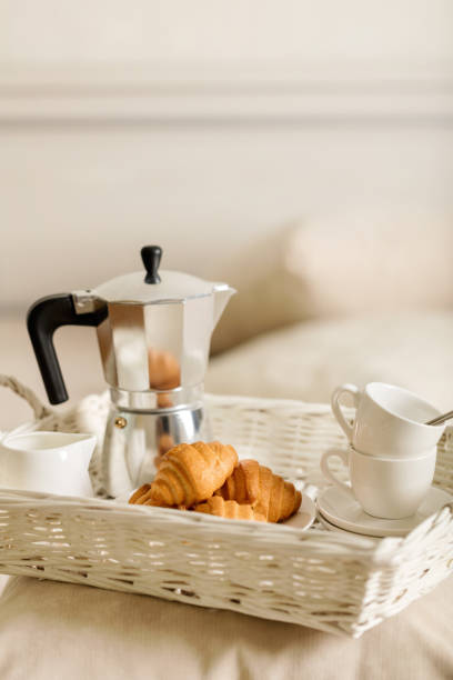 istock Breakfast in bed. On a white wicker tray there is a coffee maker, coffee white cups and croissants. 1043731574