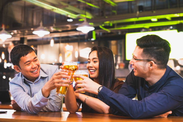 un gruppo di amici asiatici felici o colleghi di ufficio festeggiano insieme la pinta di birra tostata al ristorante del pub o al night club. dopo la festa del lavoro, l'evento di successo del team o il moderno concetto di stile di vita dell'amicizia - beer bar counter bar drink foto e immagini stock
