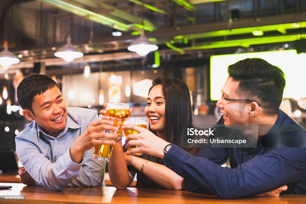 Group of happy Asian friend or office colleague coworker celebrate toast beer pint together at pub restaurant or night club. After work party, team success event or modern friendship lifestyle concept Celebratory Toast Stock Photo