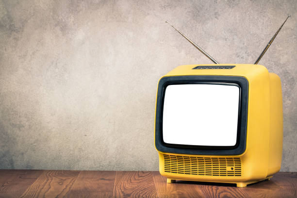 istock Retro old outdated yellow TV receiver from circa 60s on wooden table front textured concrete wall background. Vintage style filtered photo 1043734902