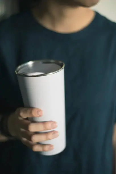 Young woman holding a tumbler, reusable coffee mug/cup in her hands.