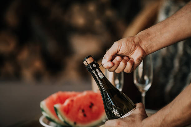 Hands open bottle of champagne. Back watermelon and fruit stock photo