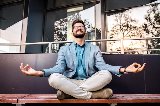 Happy young adult man in a suit meditating in front of the office