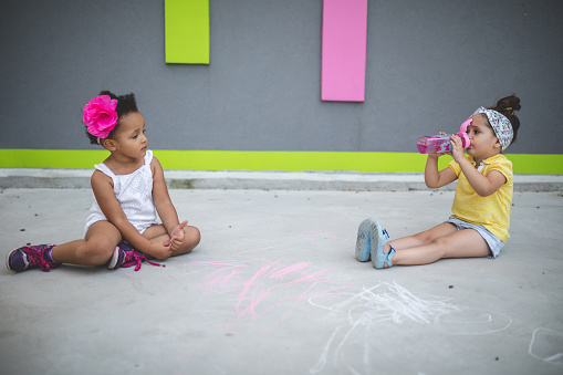 Cute and lovely mixed race siblings enjoying their time together in a city, drawing with chalk on concrete.