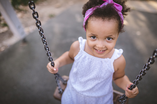 Cute and lovely mixed race child enjoying her time in a city public park, swinging on a playground swing.