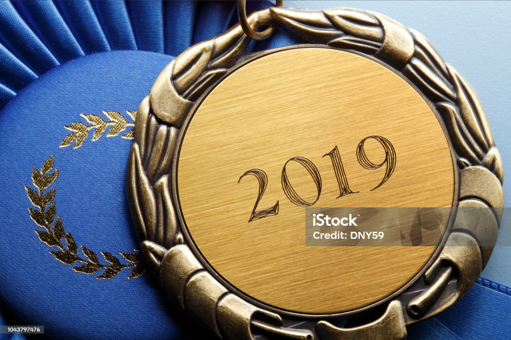 Close Up Of Medal Engraved With "2019" A close up of a gold medal engraved with the year, "2019".  The medal rests on top of a blue first place ribbon. 2019 Stock Photo