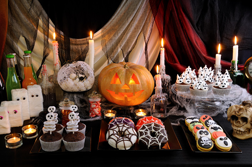 Dishes with glazed donuts, muffins with skeletons, cookies with marzipan on a Halloween table