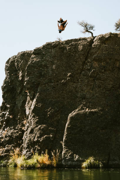 A man jumps off a high rock ledge into the river below.  Deschutes river in Oregon state, USA.