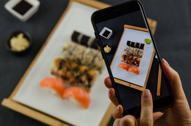 Young woman taking photo of sushi plate on smartphone. Taking food photo with mobile phone. sushi photos stock pictures, royalty-free photos & images