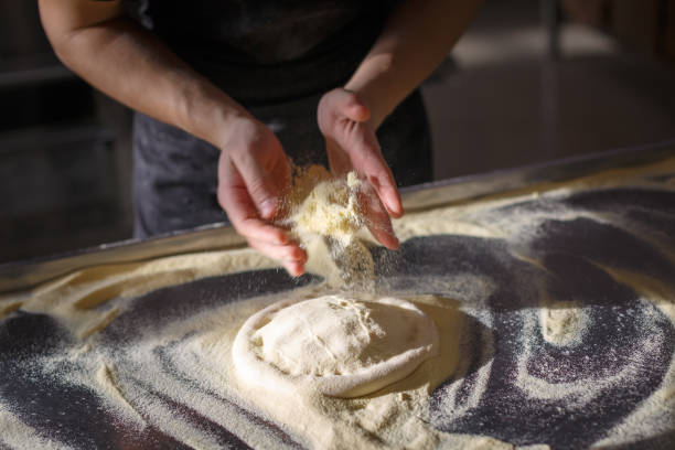 Baker sprinkles dough for pizza by semolina stock photo